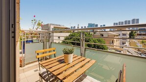 Un balcón con una mesa y banco de madera, una planta en maceta y vistas de la ciudad.