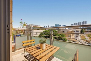 Un balcón con una mesa y banco de madera, una planta en maceta y vistas de la ciudad.