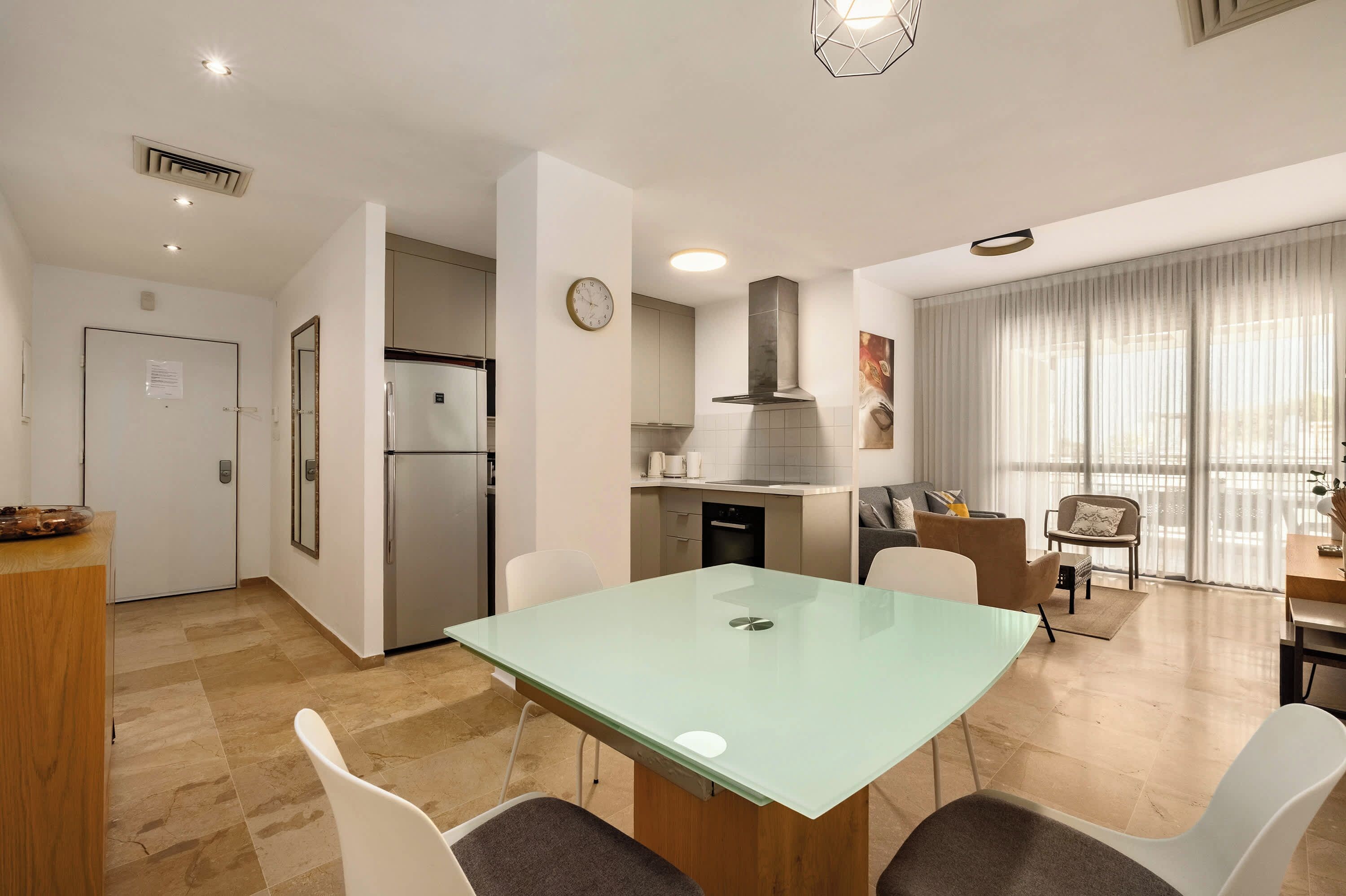 Una cocina moderna con horno empotrado, refrigerador y comedor con mesa y sillas de vidrio.