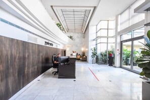 A modern reception area with a reception desk, a man sitting at the desk, and a large glass window on the right side. - Splendor 2-BR  in Melchet  by HolyGuest (Tel Aviv)