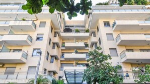 Un edificio residencial de varios pisos, con balcones, una entrada central y zonas verdes circundantes.