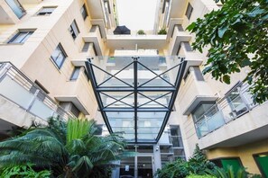Un edificio moderno de varios pisos con un amplio atrio de vidrio en el centro, rodeado de abundante vegetación.
