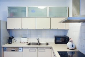Une cuisine moderne avec des meubles blancs, un lave-vaisselle, un évier, un grille-pain, une bouilloire et un four à micro-ondes.