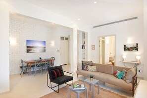 Un salon moderne avec un mur en briques blanches, un canapé, une table basse et un coin repas comprenant des chaises et une table.
