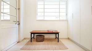 A room with a wooden bench, a woven basket, and a window with blinds. - Spacious 3BR at Mapu st by HolyGuest (Tel Aviv)