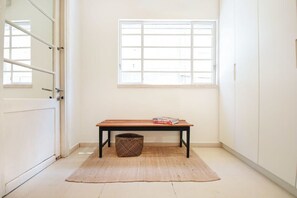 A room with a wooden bench, a woven basket, and a window with blinds.