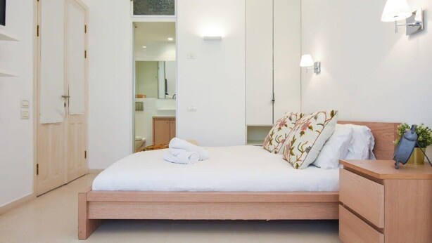 A bedroom with a bed, wooden nightstands, a wardrobe, and a mirror. - Spacious 3BR at Mapu st by HolyGuest (Tel Aviv)