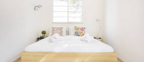 A minimalist bedroom with a wooden bed, white bedding, and a small bedside table with a plant.