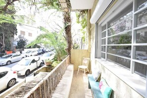A balcony with a view of parked cars, a chair, and a sofa. - Spacious 3BR at Mapu st by HolyGuest (Tel Aviv)