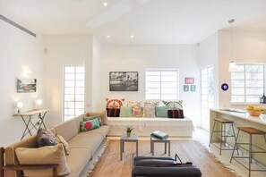 A spacious living area with a sofa, coffee table, and a dining bar with stools. - Spacious 3BR at Mapu st by HolyGuest (Tel Aviv)