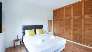 A bedroom with a large bed, wooden paneling on the wall, and a small bedside table. - Charming 2BR in Mapu  by HolyGuest (Tel Aviv)