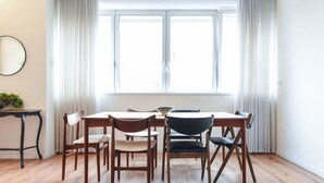 A dining area with a wooden table and chairs, a round mirror on the wall, and a window with curtains. - Charming 2BR in Mapu  by HolyGuest (Tel Aviv)