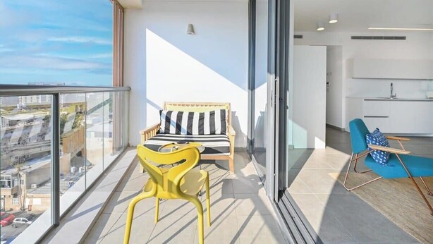 A balcony with a sofa, a chair, and a view of the cityscape.