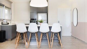 A modern kitchen with a central island, four white chairs with wooden legs, and a large pendant light. - Modern 3-BR near Beach Club by HolyGuest (Tel Aviv)