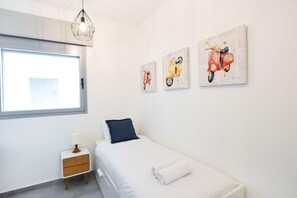 A bedroom with a bed, a nightstand, a lamp, and three wall-mounted paintings of scooters.