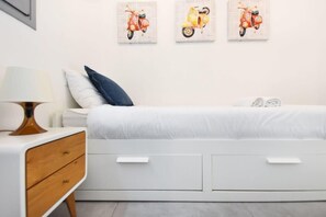 A modern bedroom with a white bed, a wooden nightstand, and three wall-mounted paintings of scooters.