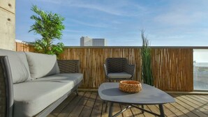 A balcony with a grey sofa, a wicker table, and a grey chair. - Modern 3-BR near Beach Club by HolyGuest (Tel Aviv)