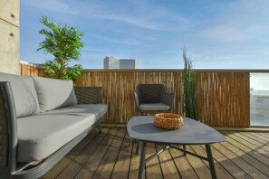 A balcony with a grey sofa, a wicker table, and a grey chair.