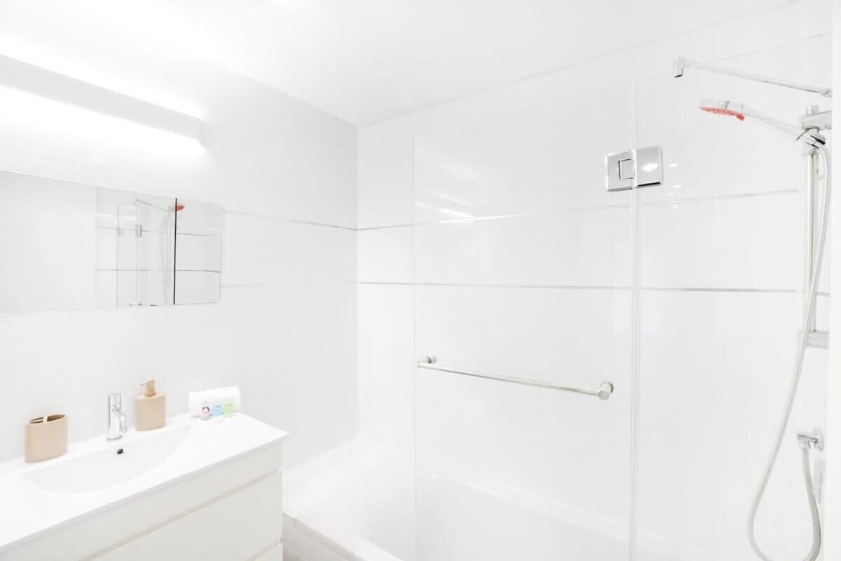 A modern bathroom with a glass shower enclosure, a white sink with toiletries, and a mirror with a towel rack.