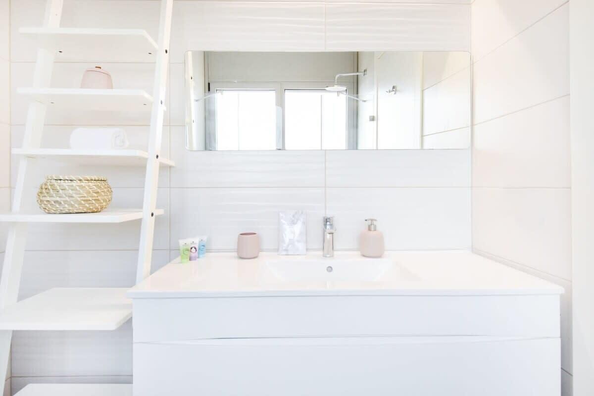 Un bany modern amb un mirall gran, un lavabo blanc i una prestatgeria amb productes de tocador.