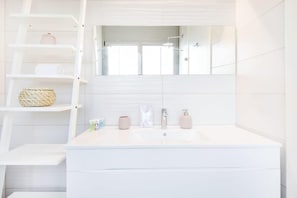 A modern bathroom with a large mirror, white vanity, and a shelf with toiletries. - Modern 3-BR near Beach Club by HolyGuest (Tel Aviv)