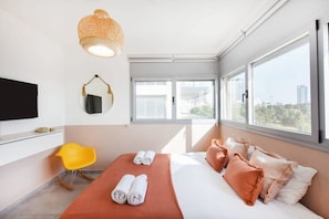 A modern hotel room with a bed, a television, a chair, and large windows.