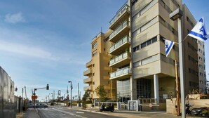 A multi-story building with balconies, a flag, and a street view. - Modern 3-BR near Beach Club by HolyGuest (Tel Aviv)