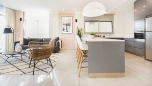 A modern kitchen with a central island, a dining area with chairs, a sofa, and a lamp. - Modern 3-BR near Beach Club by HolyGuest (Tel Aviv)