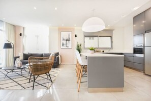 A modern kitchen with a central island, a dining area with chairs, a sofa, and a lamp.
