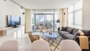 A modern living room with a flat-screen TV, a sofa, a coffee table, and a balcony with outdoor seating. - Modern 3-BR near Beach Club by HolyGuest (Tel Aviv)