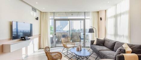A modern living room with a flat-screen TV, a sofa, a coffee table, and a balcony with outdoor seating.
