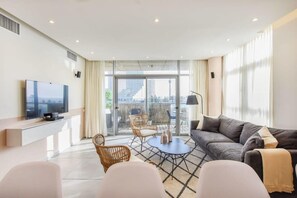 Un salon moderne doté d’un téléviseur à écran plat, d’un canapé, d’une table basse et d’un balcon avec un espace salon extérieur.