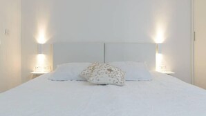 A neatly made bed with white bedding and a decorative pillow, flanked by wall-mounted light fixtures.