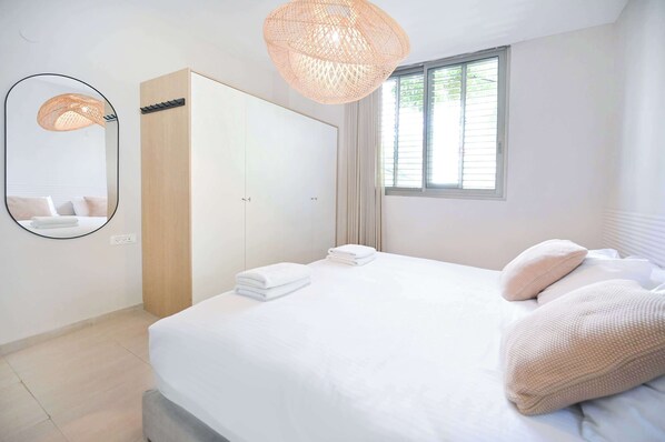 Un dormitorio con cama, armario, espejo y ventana con cortinas.