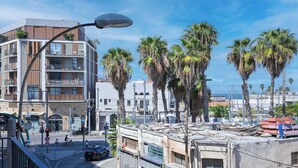 A modern building with balconies, a street with palm trees, and a clear sky.