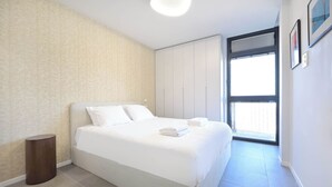 A modern bedroom with a large bed, a wardrobe, and a window providing natural light.
