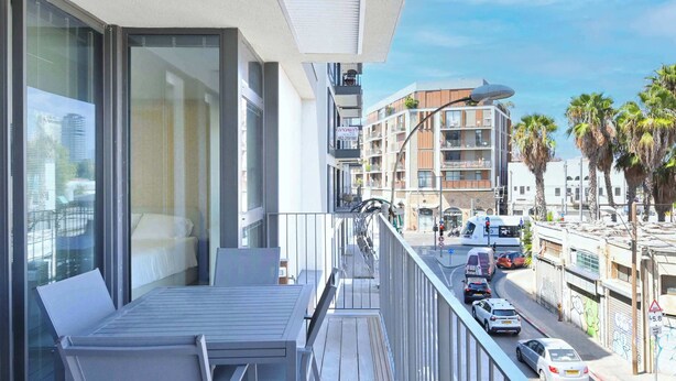 A balcony with a table and chairs, overlooking a street with cars and buildings.