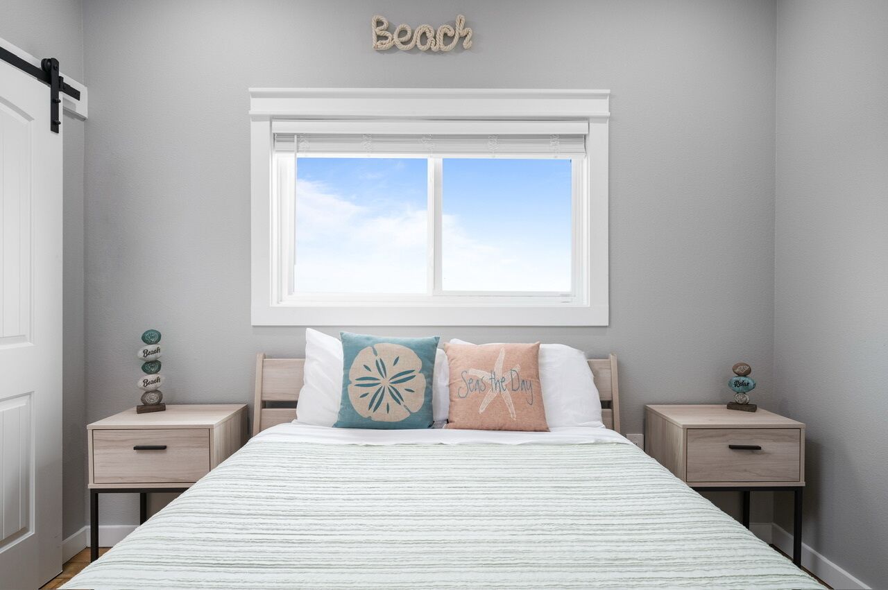 Een slaapkamer met een bed, twee nachtkastjes, een raam met uitzicht en de tekst ‘Beach’ op de muur.