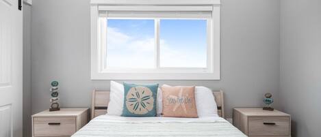 Een slaapkamer met een bed, twee nachtkastjes, een raam met uitzicht en de tekst ‘Beach’ op de muur.