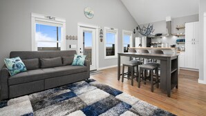 Een moderne woonkamer met een grijze bank, een blauw-wit kleed en een keuken met witte kasten en een houten eiland.