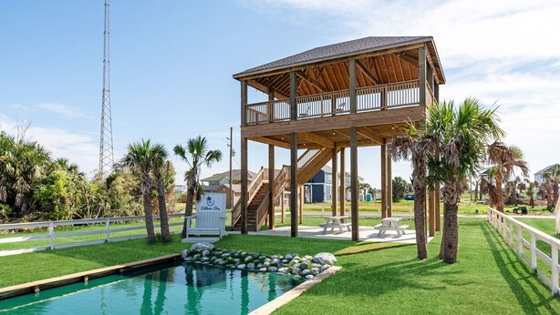Een houten constructie met een balkon, een zwembad met rotsen en palmbomen.