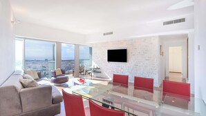 Un salon moderne avec une table à manger en verre, des chaises rouges, un canapé gris et une vue sur la ville.