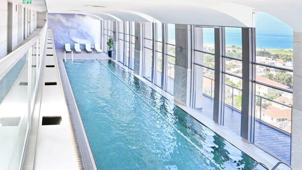 Une longue piscine intérieure offrant une vue dégagée sur l’océan et les bâtiments environnants.