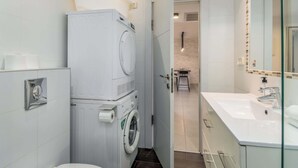 A compact hotel bathroom with a washing machine, a toilet, a sink, and a shower. - Spacious 3BR on Frishman Beach by HolyGuest (Tel Aviv)