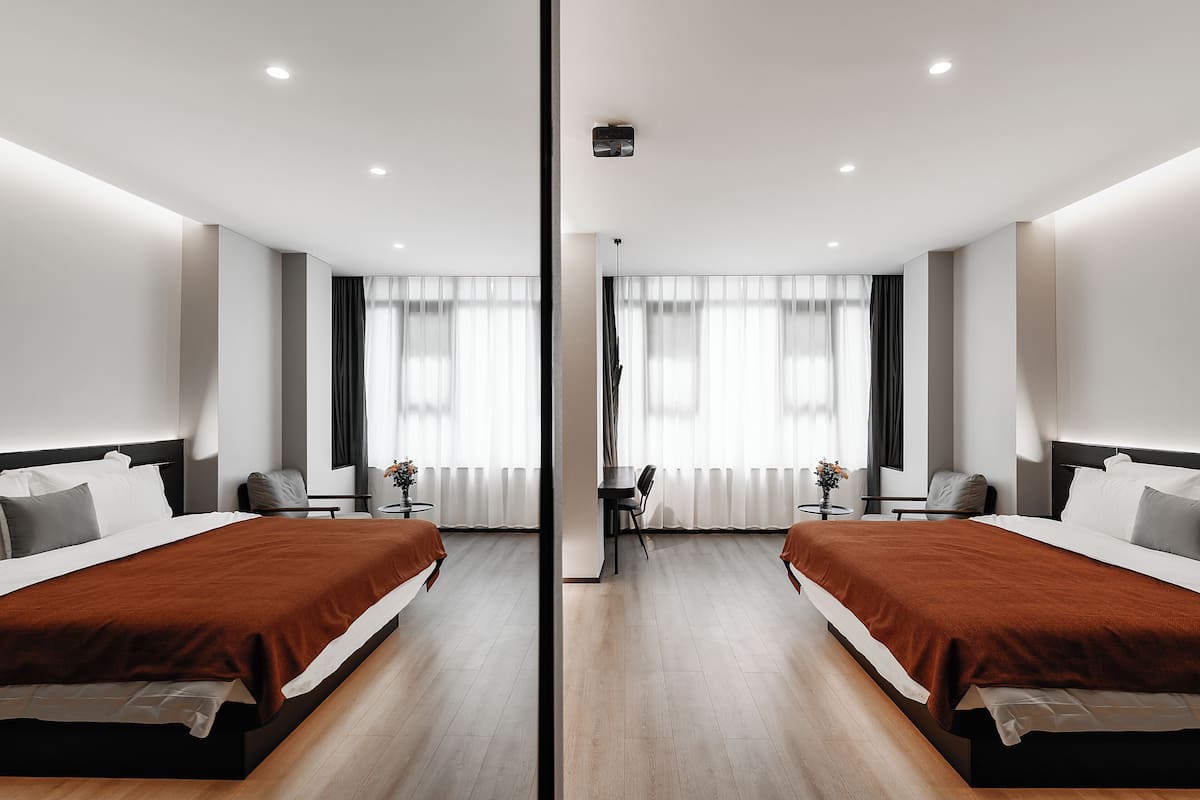 A mirrored hotel room with two beds, a small table, and a chair.