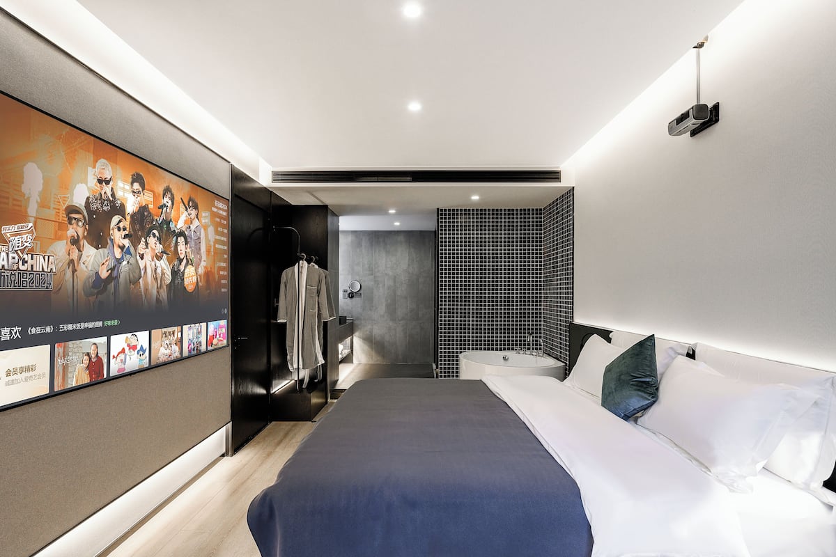 A modern hotel room with a large bed, a TV mounted on the wall, and a bathroom with a bathtub and shower.