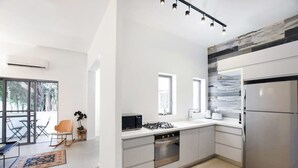 Une cuisine moderne équipée d’une cuisinière à gaz, d’un four et d’un réfrigérateur. On y trouve également un coin repas avec une table et des chaises, ainsi qu’une grande fenêtre qui laisse entrer la lumière naturelle.