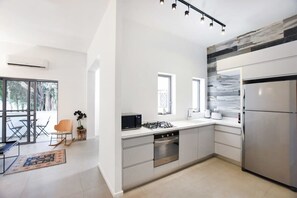A modern kitchen with a gas stove, oven, and refrigerator. There is a dining area with a table and chairs, and a large window providing natural light.