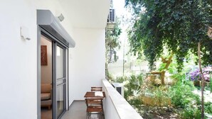 Un balcon avec une table et des chaises, une porte coulissante et une vue sur un jardin avec des arbres et des plantes.