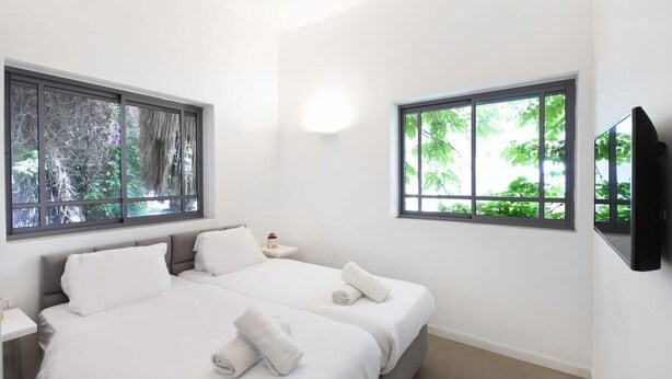 Une chambre moderne avec deux lits, de grandes fenêtres, un téléviseur à écran plat et une table de chevet.